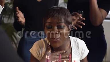 英俊的非洲女孩在生日蛋糕上和她的朋友在背景上吹蜡烛。